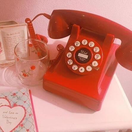 red rotary style telephone on small table. a clear glass sits next to it with a rose print